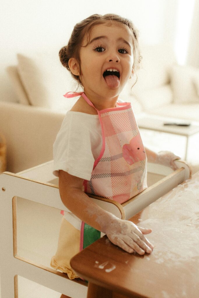 pexels-photo-35842204-35842204 A joyful child in an apron playing with flour in a warm indoor setting.