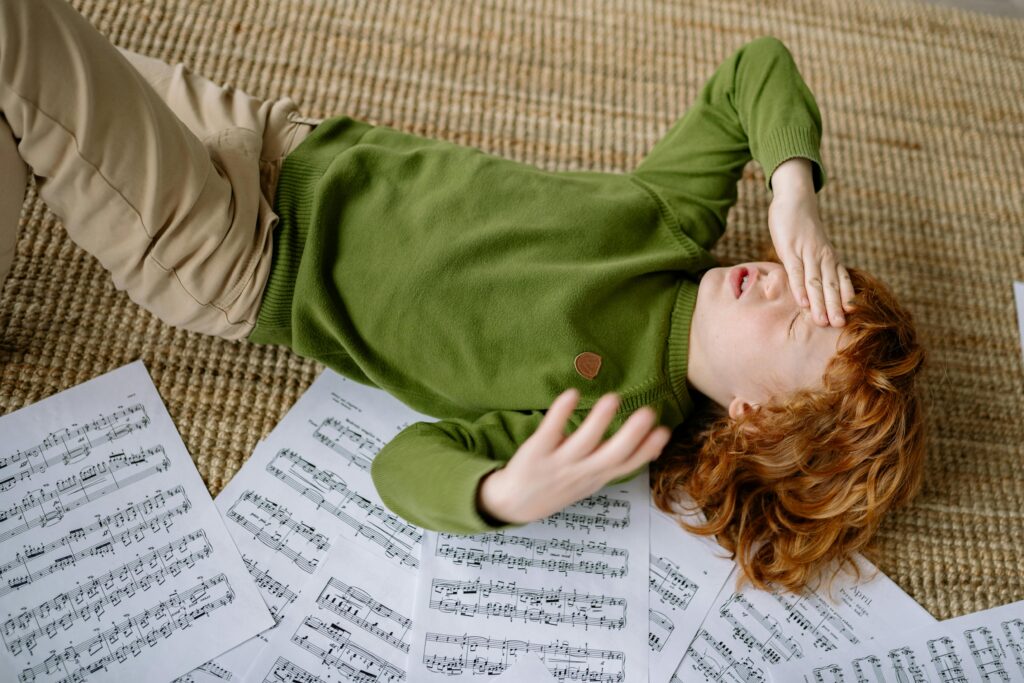 pexels-photo-8191582-8191582 A child lying on a rug surrounded by music sheets, expressing frustration.