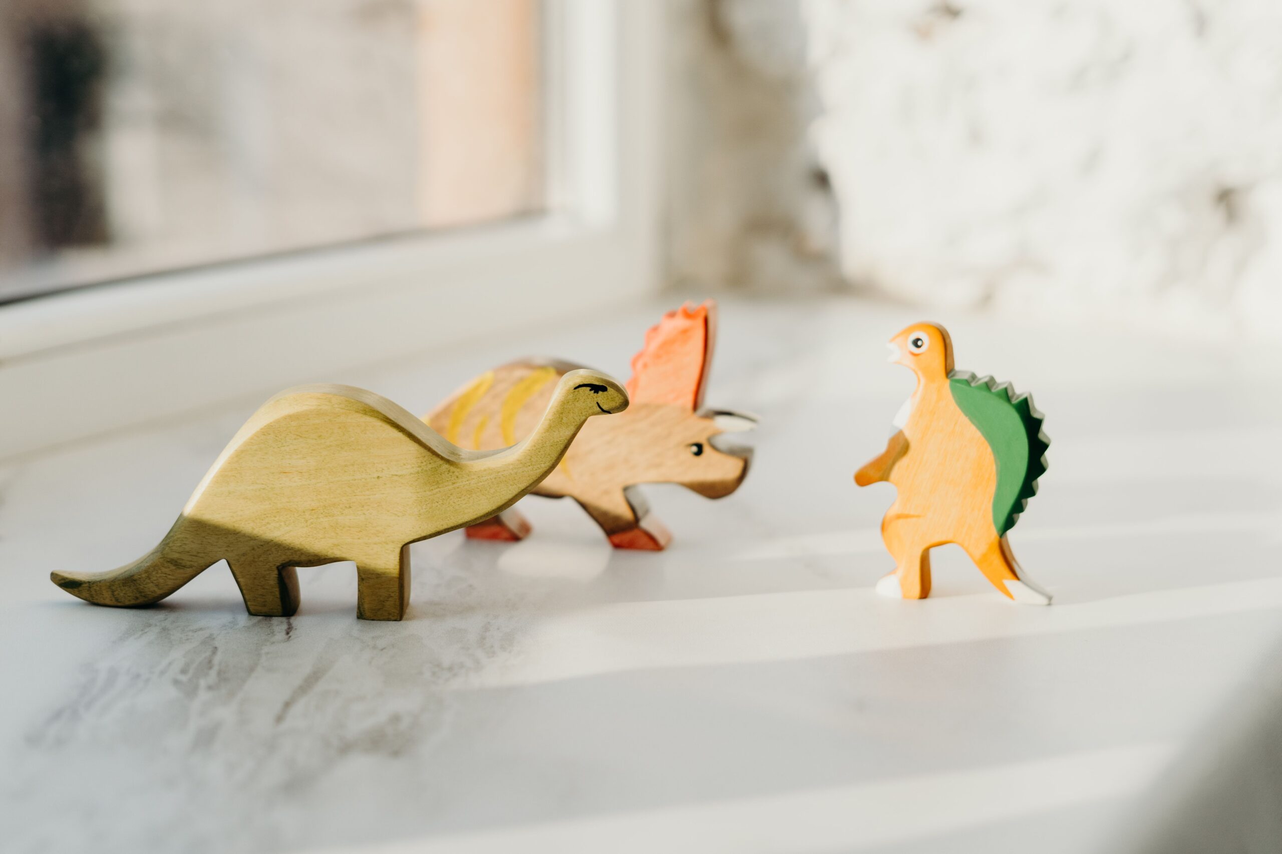 A delightful set of wooden dinosaur toys basking in natural light by the window, capturing playful innocence.