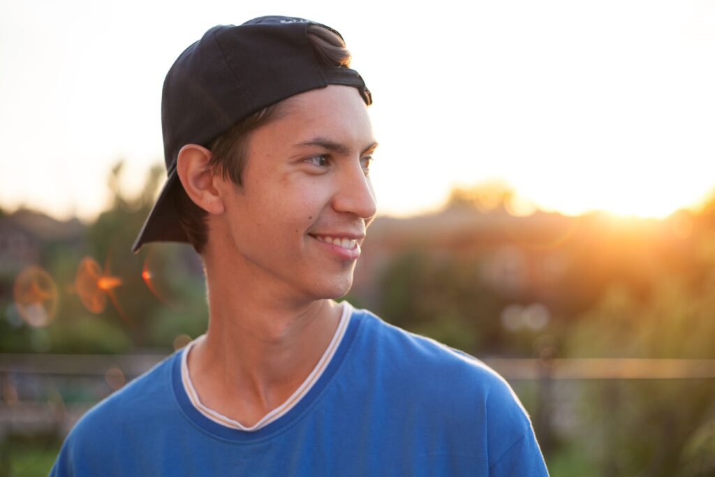 pexels-photo-7408371-7408371 Portrait of a smiling young man in a blue shirt and cap, enjoying a sunset outdoors.