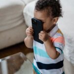 Young child playfully holding a smartphone inside a cozy home environment.
