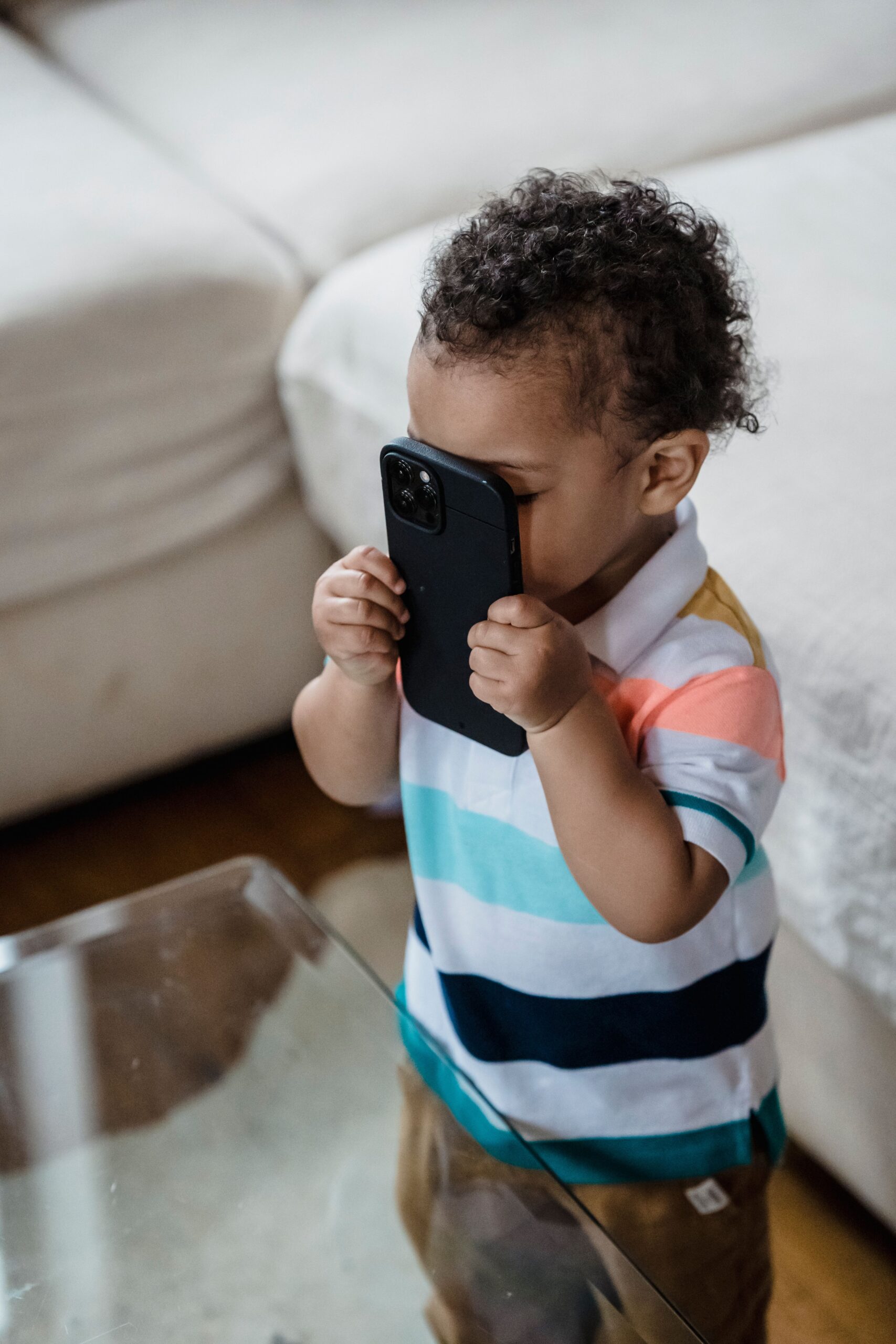 Young child playfully holding a smartphone inside a cozy home environment.