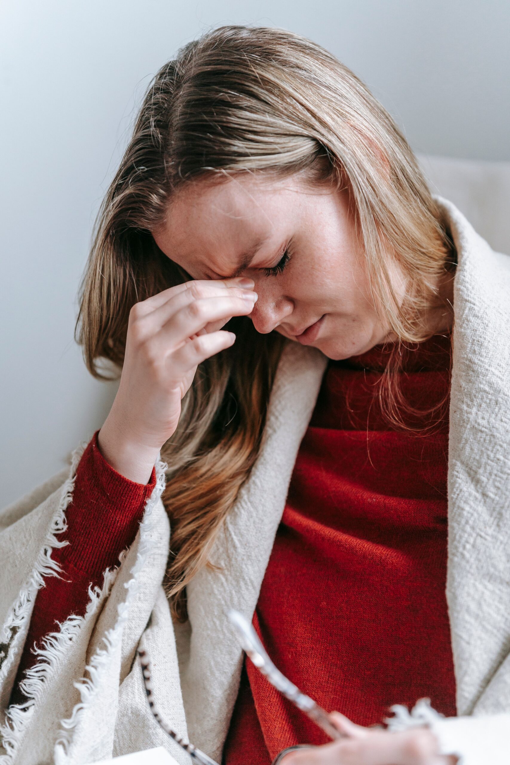 Upset serious young female with long blond hair in casual clothes touching forehead with closed eyes while resting in armchair at home